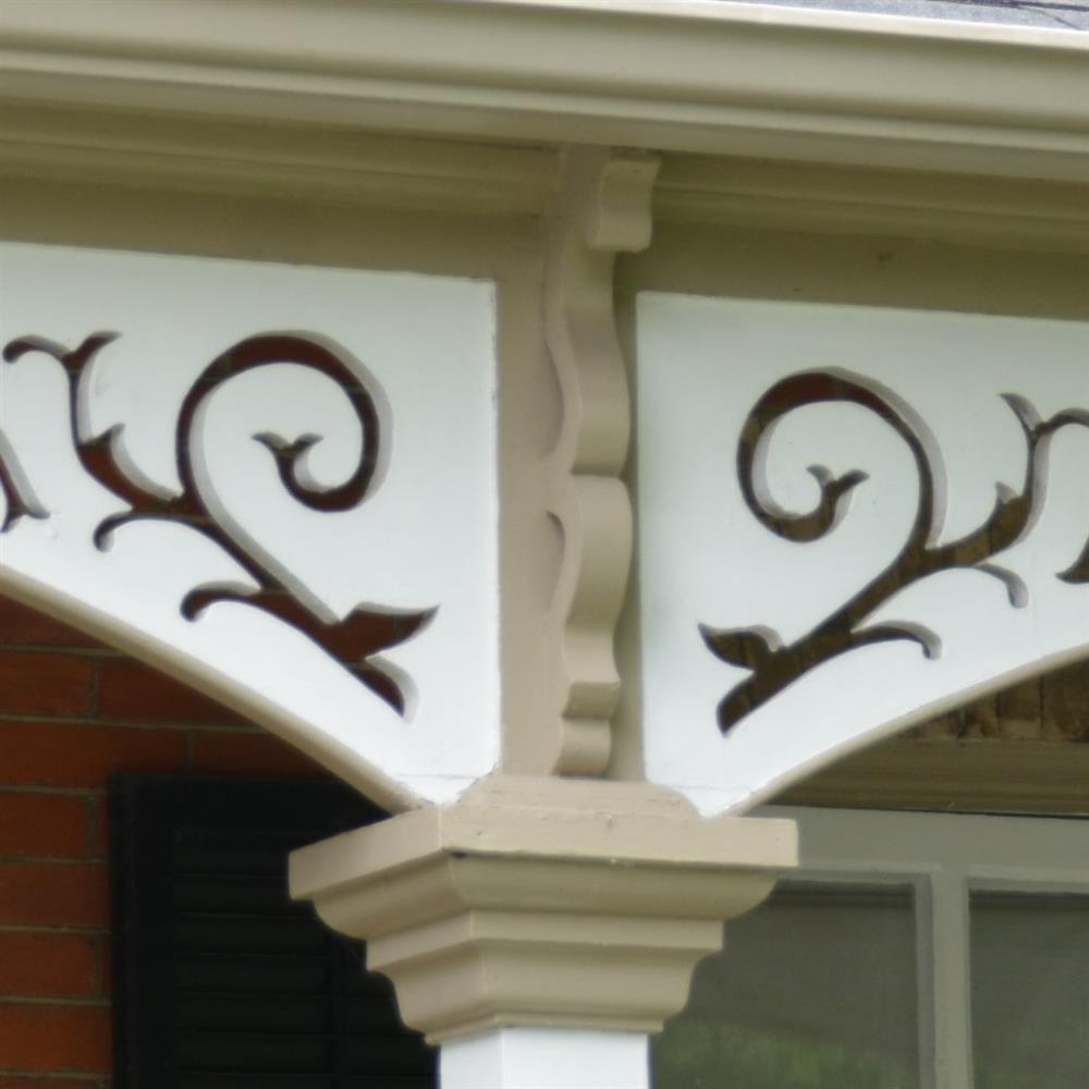 wooden triangular detail at top of a column with a botanical cut-out. White painted wood